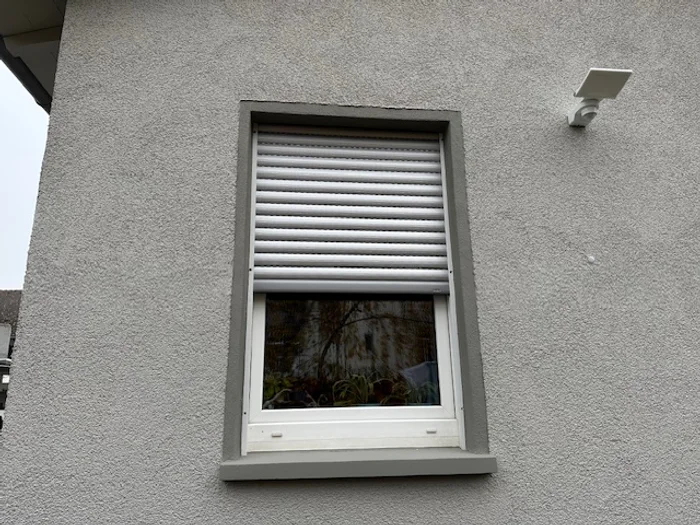 Fenster mit weißem Rollladen an einer verputzten Fassade